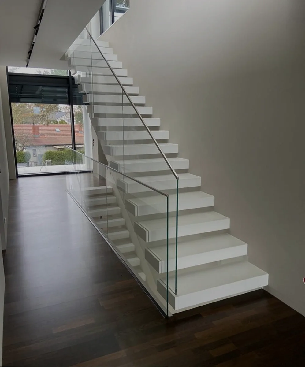 Moderne weiße Faltwerktreppe mit Glasgeländer und dunklem Parkettboden in minimalistischer Raumgestaltung